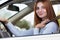 Wide angle view of young redhead woman driver fastened by seatbelt driving a car smiling happily