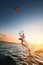 Wide angle. young caucasian woman in a wetsuit makes a trick sliding on the water against the backdrop of a sunset in