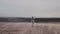 Wide background shot, young female tourist struggles to walk under extreme wind on sand dunes in Scandinavia slow motion