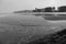 Wide beach of Northern sea with storm waves on cloudy winter day. Buildings along seacoast black and white.