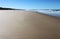 Wide beautiful expanse of beach in foreground with waves coming in and people tiny in and near the water in the background