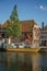 Wide canal with brick houses, boats moored on its bank reflected in water and blue sky of sunset in Weesp.