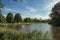 Wide canal with grove, green bushes and blue sky at sunset in Weesp.