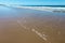 Wide expanse of wet beach with water retreating and low waves coming in and foam and water on the beach and reflection of turqoise