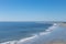 Wide flat beach on blue ocean waters, small waves and distant beachcombers, blue sky