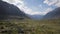 The wide green mountain valley with stones on the ground and high rocky hills arround.