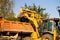 A wide metal excavator bucket digs sand or clay and loads it into a dump truck at a construction site