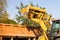 A wide metal excavator bucket digs sand or clay and loads it into a dump truck at a construction site