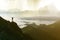 Wide mountain panorama. Small silhouette of tourist with backpack on rocky mountain slope with raised hands over valley covered