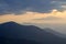 Wide panorama, fantastic view of covered with morning mist green Carpathian mountains at dawn under dark clouds and light pink sky