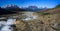 A wide panorama of the mountain landscape with snowy peaks, a bubbling mountain river flowing down the valley among stones and