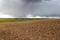 Wide panorama of plowed empty field before planting stretching to woody hills and distant village on horizon under dramatic cloudy
