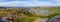 Wide panorama view from above of a rock cliff and the ocean, green valley and small village in Norway. Valoy. Vikna Green grass