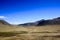 Wide panoramic view of a dry barren desert land with roads mountains and blue sky