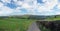 A wide panoramic view of yorkshire dales countryside with a narrow country lane with stone walls and fences around grass meadows