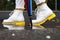 A wide photo of a woman`s boot walking in a puddle on the road in autumn with many colorful leaves.