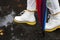 A wide photo of a woman`s boot walking in a puddle on the road in autumn with many colorful leaves.