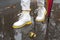 A wide photo of a woman`s boot walking in a puddle on the road in autumn with many colorful leaves.