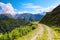 A wide road with a cliff leads down to the high Caucasus mountains.