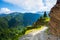 A wide road with a cliff leads down to the high mountains.