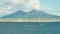 Wide screen view on volcano Vesuvius in Naples Italy offshore. Blue sky and clouds above volcano, surfers in ocean under volcano.