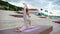 Wide shot of attractive slim sporty woman sitting on twine with arms up on yoga mat outdoors.