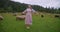 Wide shot barefoot beautiful Ukrainian woman in national dress standing on mountain meadow with sheep walking at