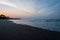 Wide shot of the beach with fine sand and tree and waves crashing into the shore during sunset