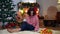 Wide shot bored woman sitting on Christmas eve at home alone with book and tea cup sighing looking away. Portrait of sad