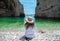Wide shot of a brunette sitting at a beautiful beach at Stiniva bay, island of Vis in Croatia. Teal green clear sea, blue sky and