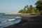 Wide shot of canoes on a brown sandy shore by the sea surrounded by tropical trees