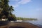 Wide shot of canoes on a brown sandy shore by the sea surrounded by tropical trees under a blue sky