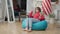 Wide shot of carefree Asian teenage girl entering room and sitting down on bag chair. Portrait of relaxed redhead