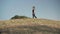 Wide shot of Caucasian female gymnast walking along hill and jumping up raising leg up. Side view portrait of flexible