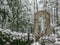 Wide shot of a cemetery with a big concrete cross sand tall trees all over the area on a snowy day