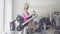 Wide shot of charming blond sportswoman exercising in sports club on equipment. Side view portrait of young slim