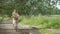 Wide shot of charming young Caucasian woman riding bike in summer park. Portrait of smiling positive slim lady in dress