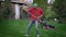 Wide shot of cheerful young man raking and imitating playing guitar on rake singing and smiling. Portrait of funny