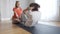 Wide shot of cute positive girl holding feet of boy pumping press on exercise mat. Portrait of Caucasian sister helping