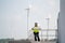 Wide shot of engineer or technician woman worker hold drawing paper and stand on base of windmill or wind turbine and look at