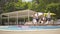 Wide shot of four sportive athletic men passing by slim beautiful women sitting on sunlounges at poolside. Portrait of