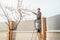 Wide shot of a gardener treating a fruit tree with a sprayer standing on the ladder
