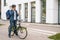 Wide shot of handsome bicycle courier male with thermal backpack talking on mobile phone to customer, looking for