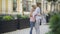 Wide shot of happy Caucasian grandmother and granddaughter hugging on city street. Side view portrait of happy senior