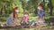 Wide shot happy Caucasian siblings sitting on spring summer picnic in park talking. Relaxed redhead boys and girl in