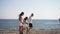 Wide shot of happy family holding hands strolling in sunshine on rocky Mediterranean sea coast. Side view of father with