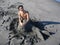 Wide shot of a happy male sitting on a black sand shore with a mermaid tail made of sand