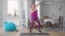 Wide shot of hilarious obese woman grimacing stretching resistance band training at home. Portrait of funny Caucasian