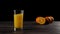 Wide shot of ice cubes falling in a tall glass with fresh orange juice making splashes and bubbles on a wooden table