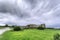 Wide shot of isolated abandoned building ruins in a green field under the dark cloudy sky
